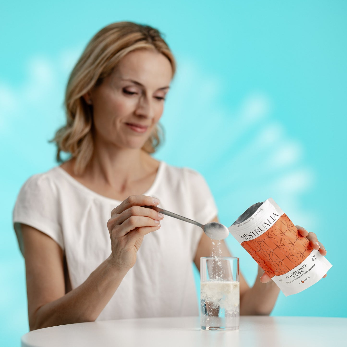 Woman pouring powder from a container into a glass with a blue background